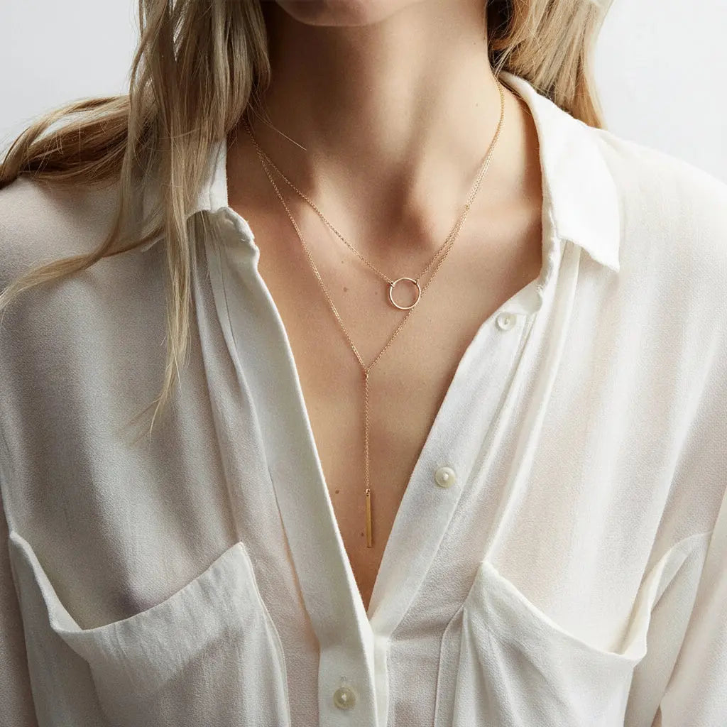 Person wearing a gold necklace with a minimalistic design.