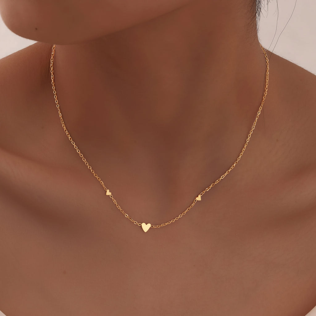 Gold necklace with heart pendants on a person's neck against a neutral background