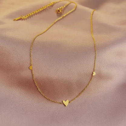 Gold necklace with a heart pendant on a soft pink background