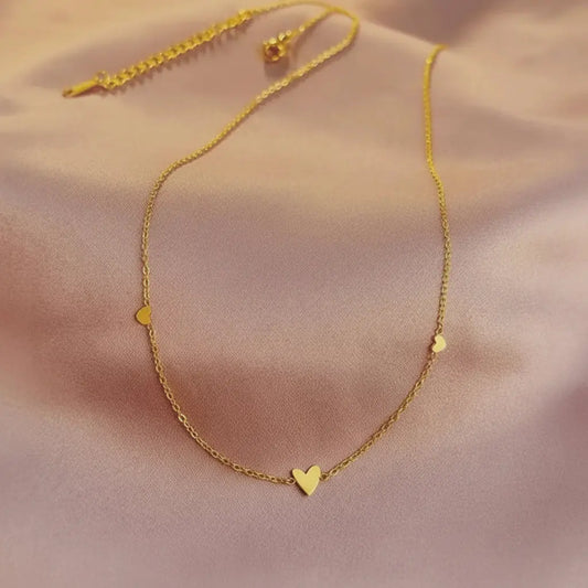 Gold necklace with a heart pendant on a soft pink background