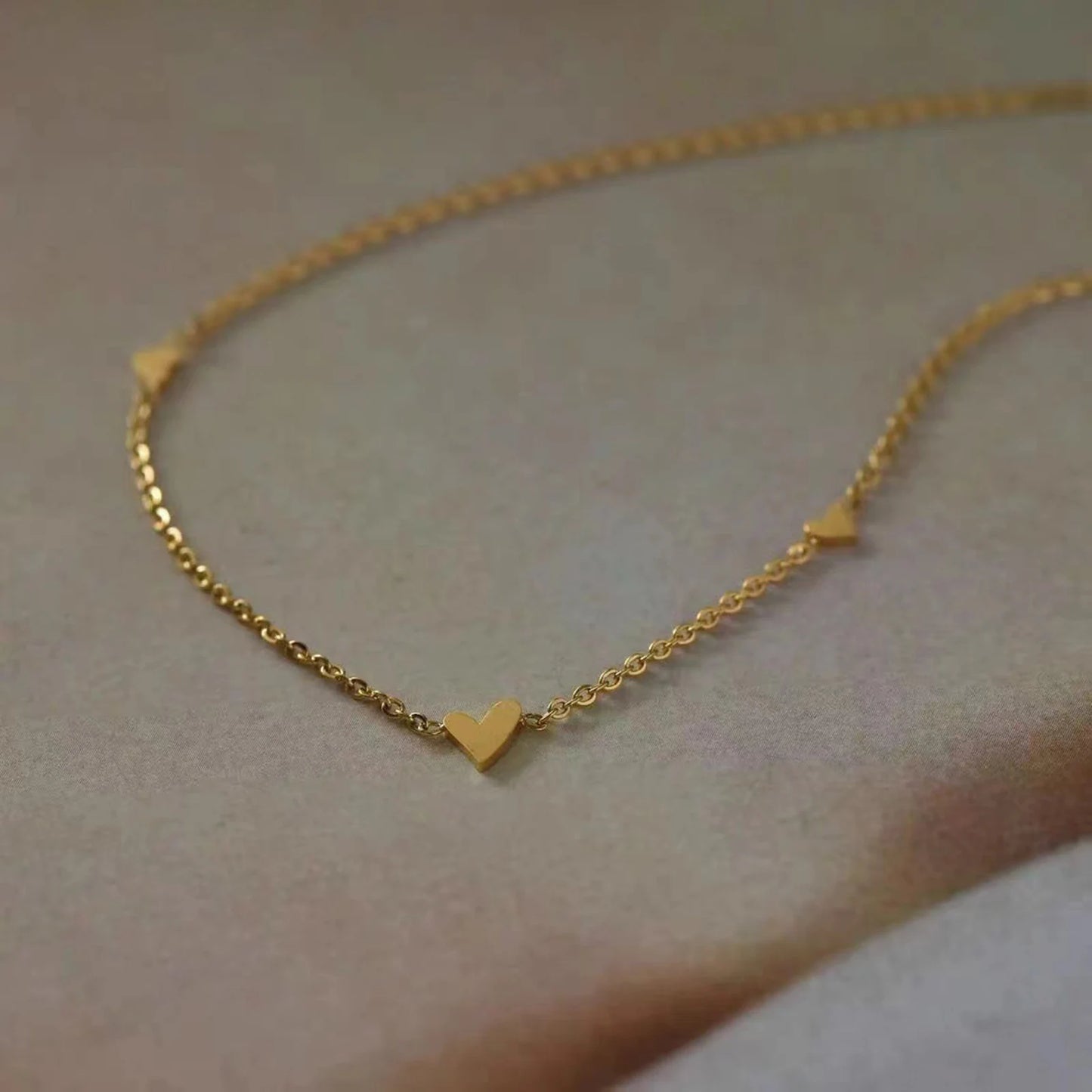 Gold necklace with heart-shaped pendants on a neutral background