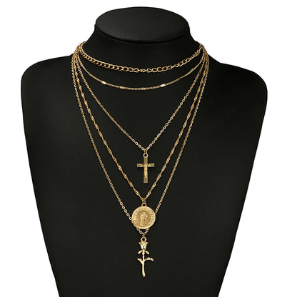 A gold layered necklace set displayed on a black mannequin bust against a white background. The set includes multiple chain layers, a small cross pendant, a round medallion pendant, and a rose charm.