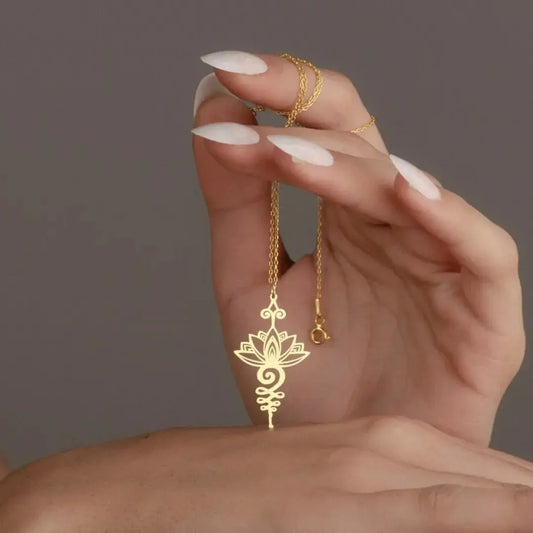 Gold necklace with a lotus pendant held by a hand against a neutral background
